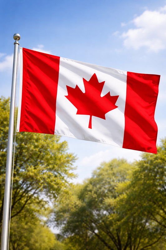 Canadian flag waving in the wind against a blue sky with trees in the background