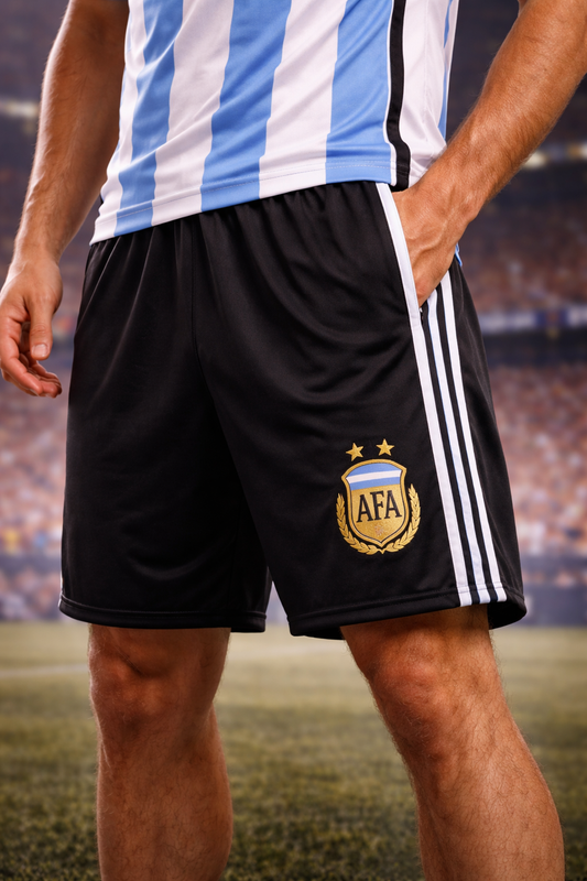Person wearing black soccer shorts with AFA logo and blue and white striped shirt on a blurred stadium background
